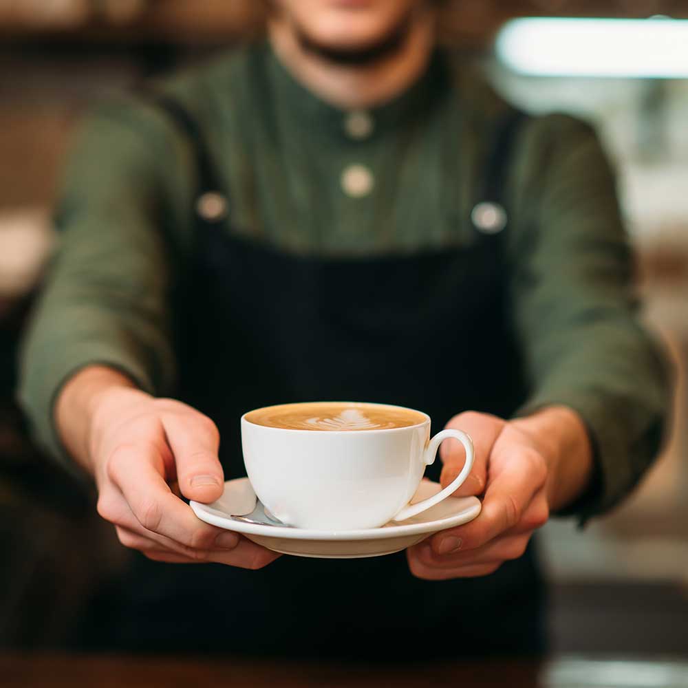 Kellner in schwarzer Schürze streckt eine Tasse Kaffee aus